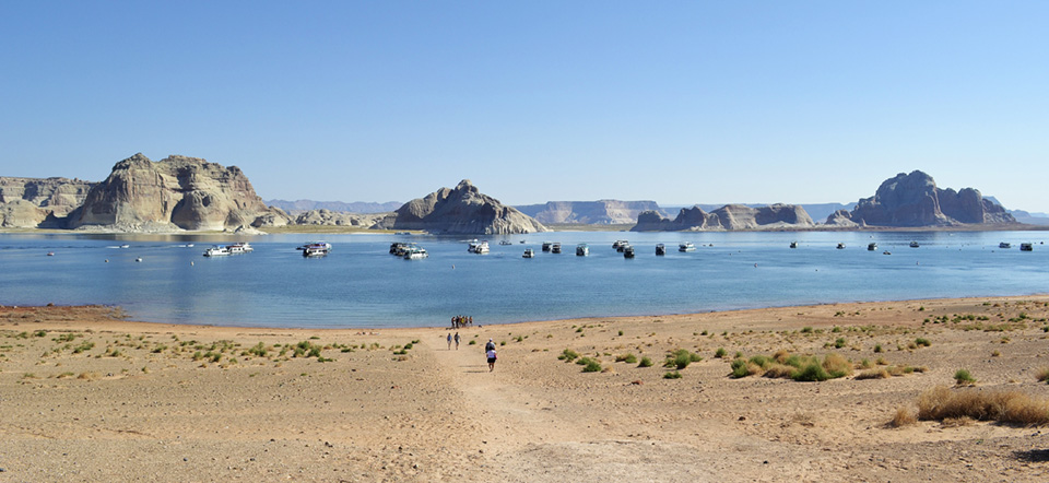 groups of people and vehicles on beach, lake, sandstone cliffs.