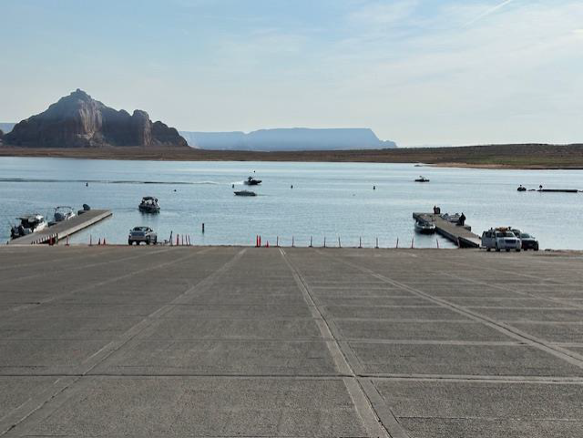 Wahweap Main Ramp, Lake Powell at lake elevation 3554.03 ft. on August 7, 2025 A concrete launch ramp ending in a desert lake. Boats are docked below the ramp and floating in the lake. Trucks are parked on the ramp.