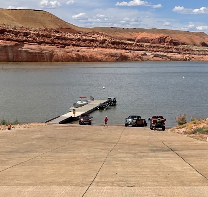 Hall Crossing May 2023 Pick up trucks hauling boats launch at the end of a paved boat ramp at waters edge.