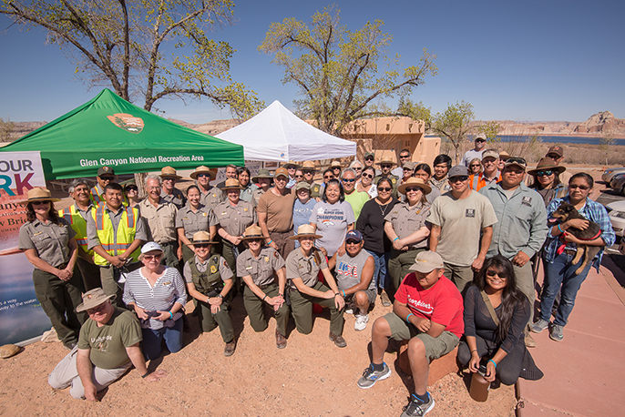 Lalarge group of people, including rangers facing the camera. pop up tents in the background, Lake Powell in the far background.