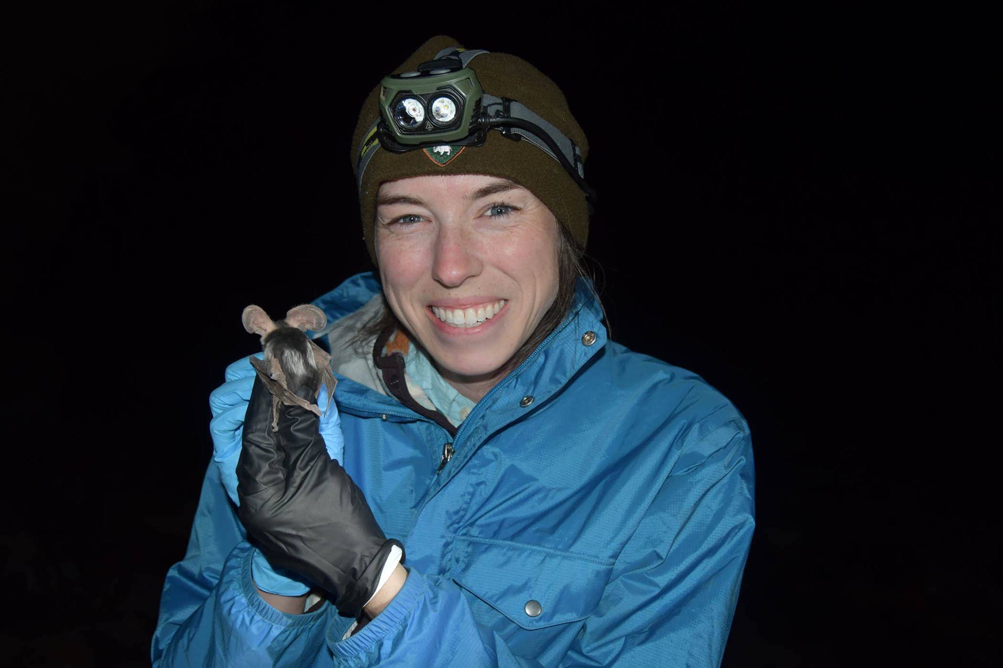 Grinning researcher shows off spots on back of bat she is handling