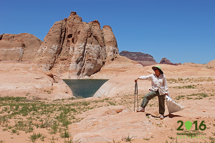 Woman with trash bag and grabbers looks at the sandstone and lake scenery.