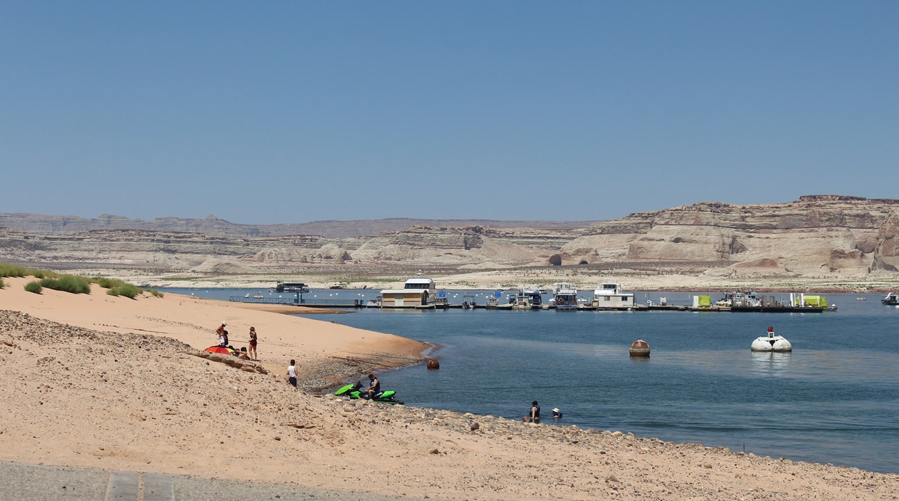 Desert beach with people swimming, on boats, and on the beach.