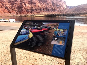 Information about river running on a wayside panel placed near river with truck unloading boats in background