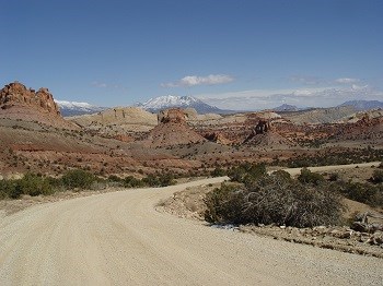 Dirt road winds past colorful buttes with snowy mountain in distance Dirt road winds past colorful buttes with snowy mountain in distance