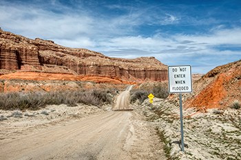 Dirt road. Sign reads "DO NOT ENTER WHEN FLOODED". Creek runs across the road.