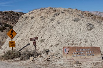 road signs indicating the boundary of Capitol Reef National Park, trailhead register, and slippery when wet road