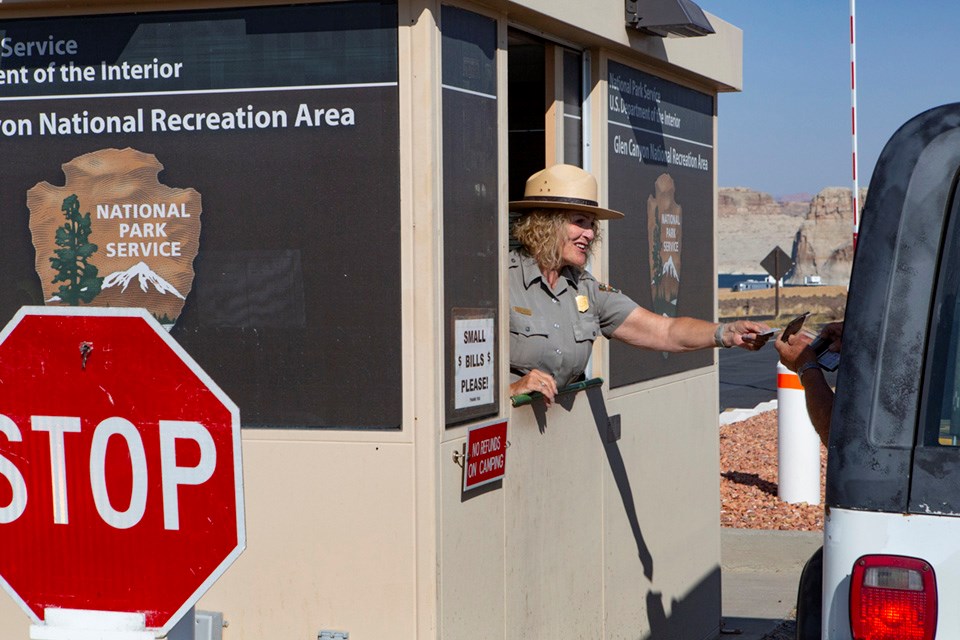Park ranger reaches out of booth to as vehicle