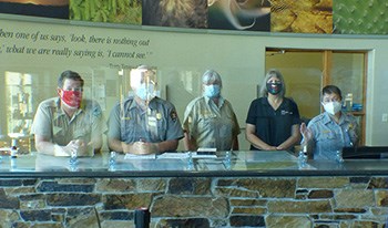 five people wearing face masks standing behind plexiglass