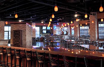 Lights dangle above tables and bar in large open restaurant