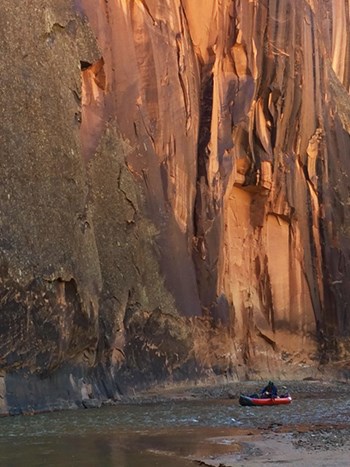 Kayak navigates riffle below towering sandstone canyon wall