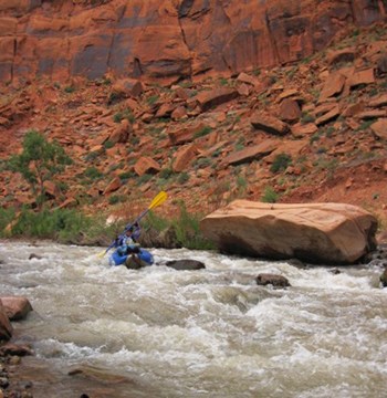 Kayaker maneuvers past rock in rapid