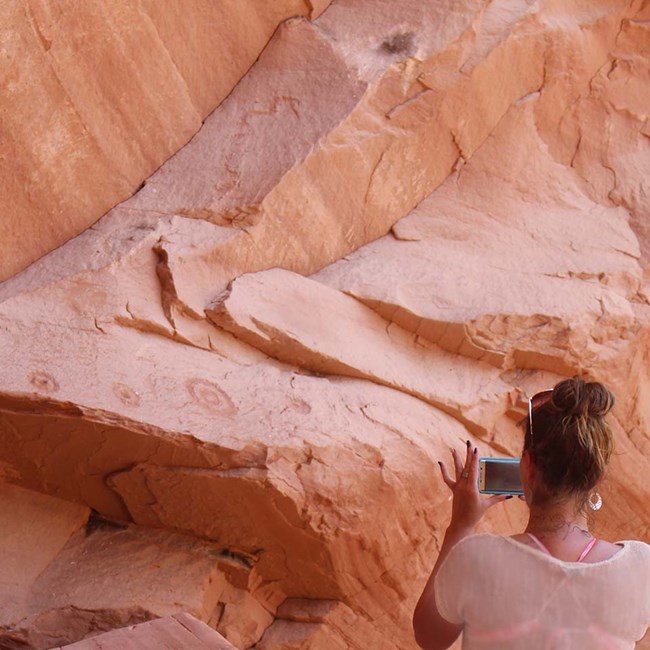Woman takes photos of native petroglyphs on a canyon wall