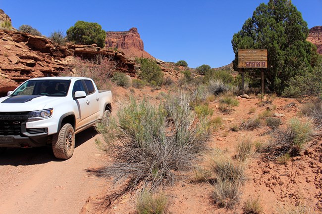 Truck parked on dirt road amongst sandstone cliffs