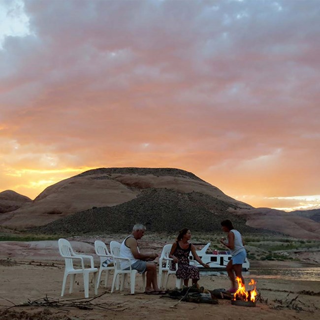 Three people around a beach campfire in the evening at Lake Powell