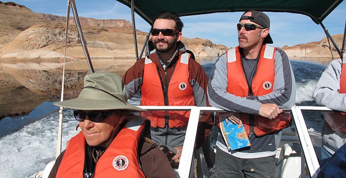 Three people wearing lifejackets are on a boat traveling across Lake Powell. Three people wearing lifejackets are on a boat traveling across Lake Powell.