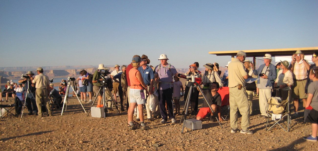 Large group of people standing in a row with telescopes on tripods.