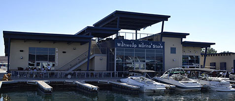 A beige building with blue trim with the sign, "Wahweap Marina Store." Three boats are docked in front of the building. A beige building with blue trim with the sign, "Wahweap Marina Store." Three boats are docked in front of the building.