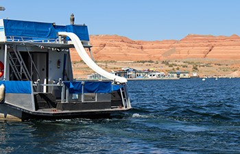 The back end of a houseboat with a slide into water; marina in background