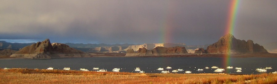 Panoramic view of houseboats on lake Powell. A double rainbow arcs over the scene.