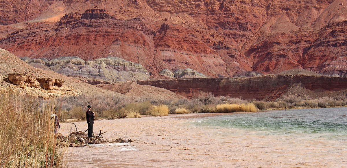 Fisherman stands on shore where the muddy Paria flows into the Colorado River