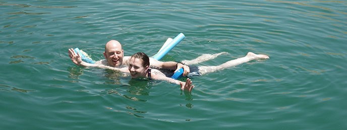 A man and a woman swimming with two long swim noodles. A man and a woman swimming with two long swim noodles.