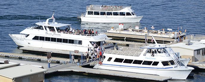 Three large white boats full of people at a dock. One boat is departing. Three large white boats full of people at a dock. One boat is departing.