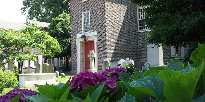 Close-up of a flowering bush. A brick church and burial ground in the background. Close-up of a flowering bush. A brick church and burial ground in the background.