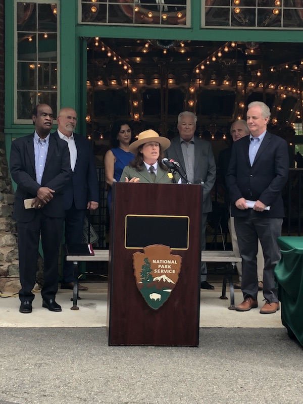 Ranger speaks at a podium with local officials and historic carousel in the background.