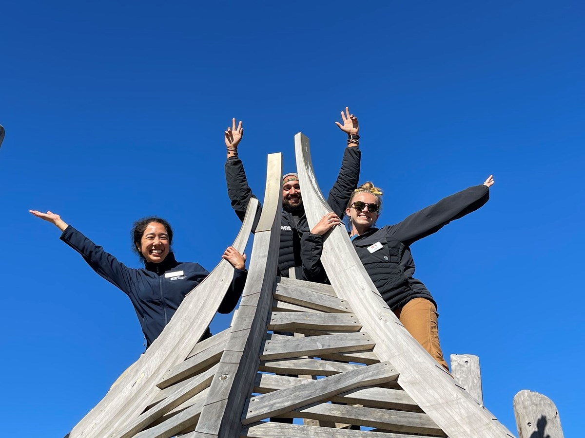 Two Academic interns with a Presidio Trust staff up top a play structure with their hands up in the air!