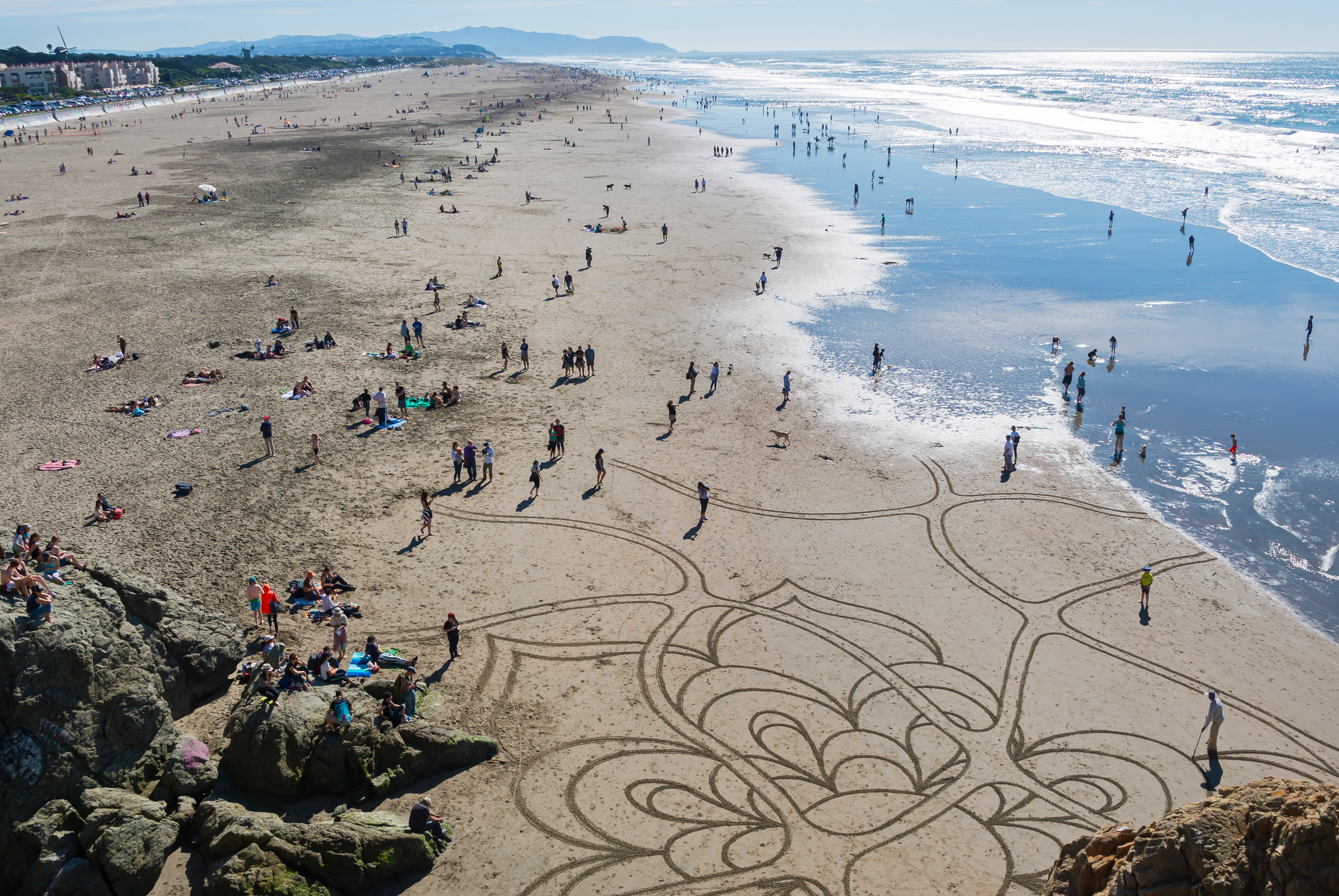 Sand art on Ocean Beach View of ocean beach crowds on a beautiful day, including someone creating sand art with a rake, from an overlook at the beach's north end