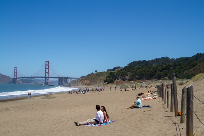 People sit on a beach near the Golden Gate Bridge