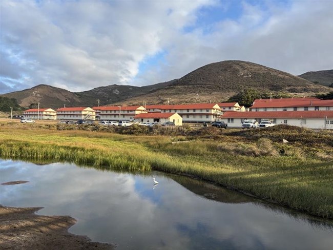 Clouds reflect on the lagoon in front of rows of buildings.