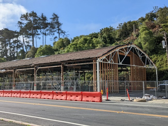 Color picture of Presidio building PE-643 rehabilitation project. Brown roof and supporting beams visible with orange barricades in front of building.