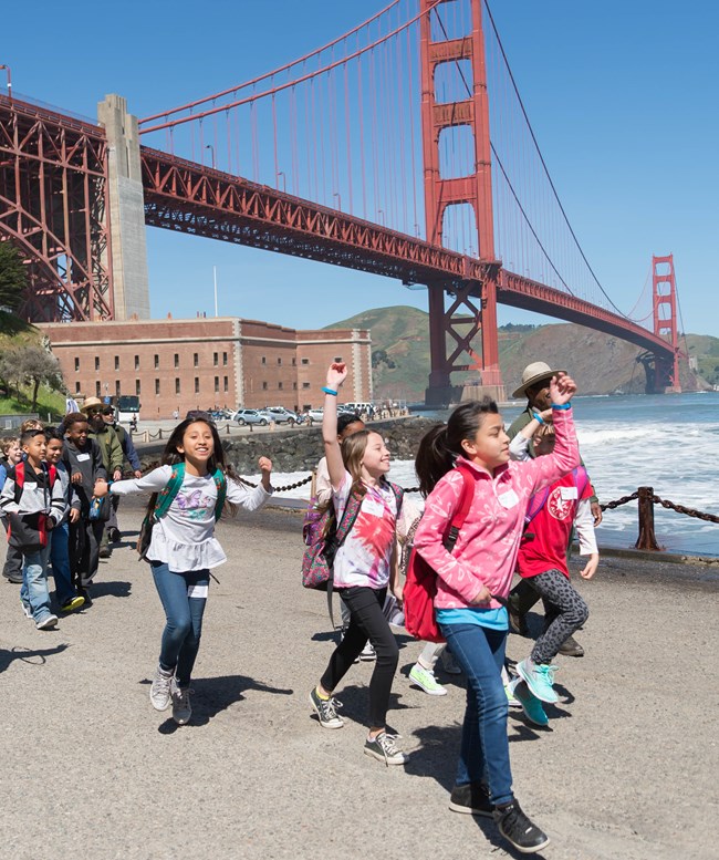 group of kids walk down road in front of Fort Point and Golden Gate Bridge group of kids walk down road in front of Fort Point and golden gate bridge