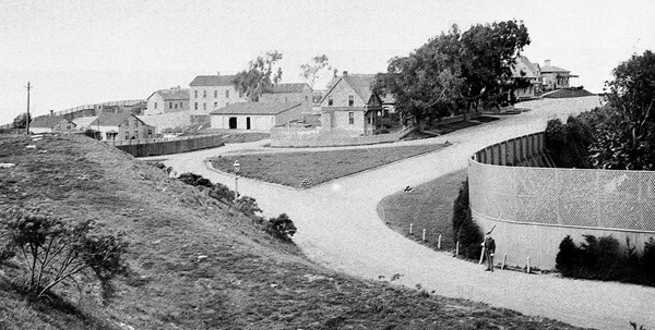 historic image of Fort Mason with soldier at attention in front of wood-frame buildings