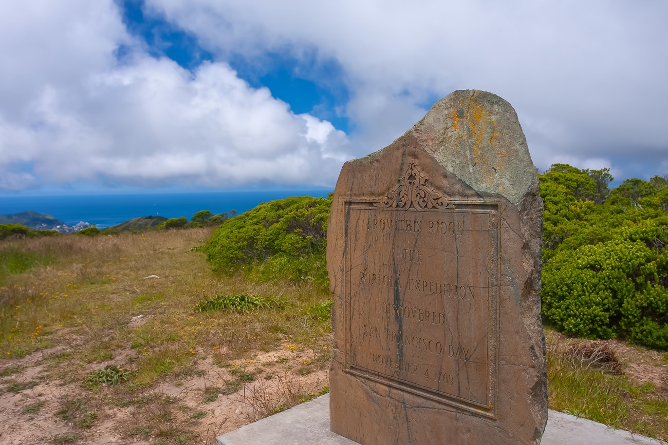 Inscribed serpentine rock monument at top of Sweeney Ridge, with ocean in the distance behind.