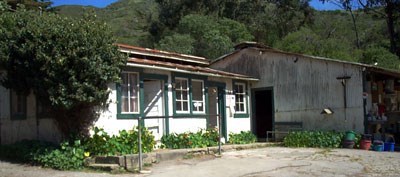 small white building with green trim in front of metal barn