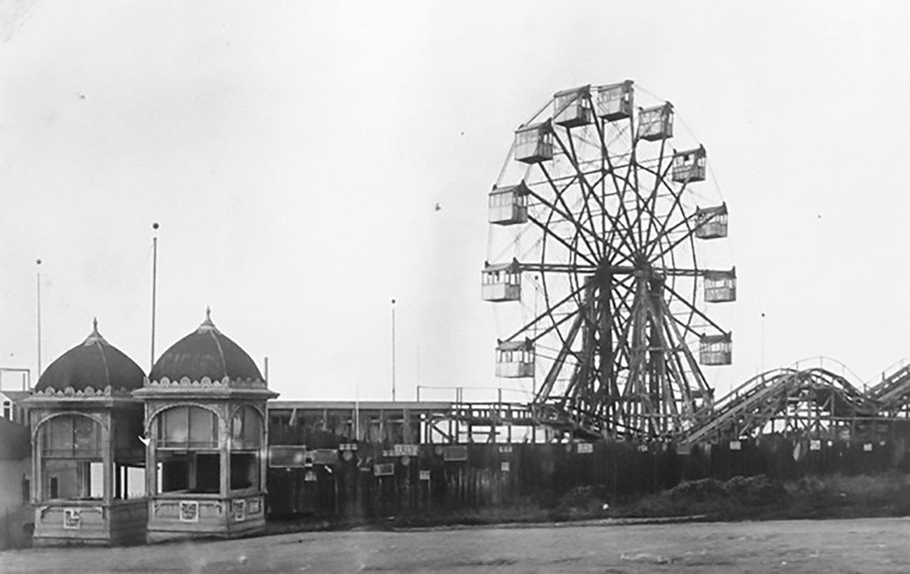 historic photo of ferris wheel, low rollercoaster and decorative ticket booths.