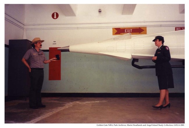 Lt. Susan P. Cheney and Ranger John Martini Susan Cheney speaks with Ranger John Martini. They are underground in a missile sile, and a Nike missile is behind them.