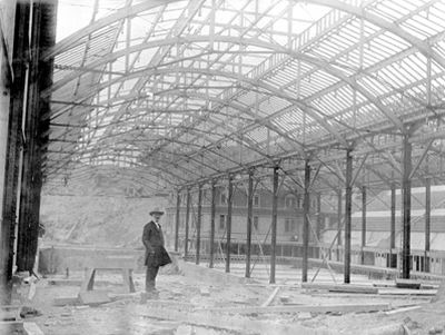 Men in hat standing in middle of uncompleted cast iron building.