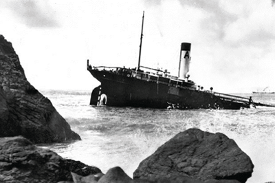 Large ship half submerged in water with surf and rocks nearby. Large ship half submerged in water with surf and rocks nearby.