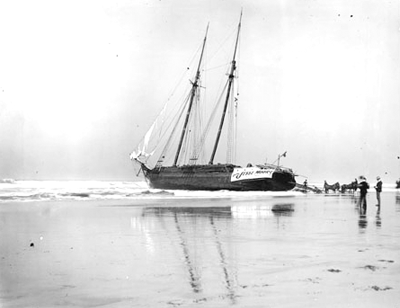Wooden ship with masts listing to one side, stuck on a beach.