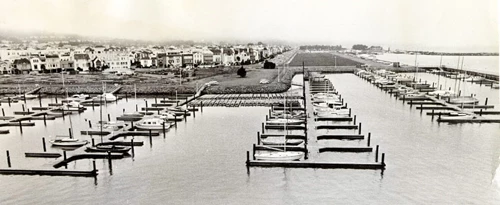boat slips in small harbor with residential buildings in background