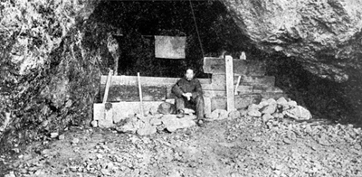 Man sitting in cave among wooden planks.