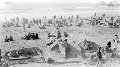 Large group of people standing on Ocean Beach around ornate three-dimensional sand sculptures.