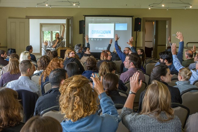 A crowd raises their hands as a ranger presents on sustainability in GOGA.