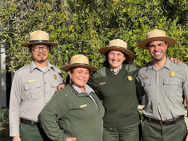 Four park rangers stand in front of a leafy green background