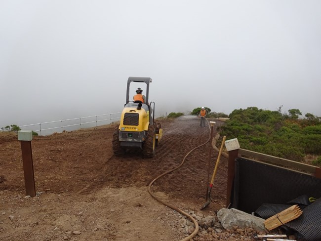 A person operates construction equipment along a Hawk Hill trail on a very foggy day.