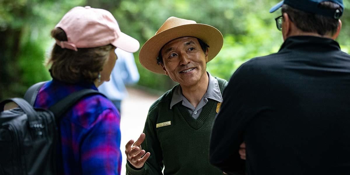 A ranger in a flat-hat speaks to two visitors